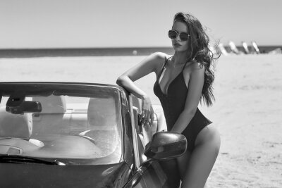 sexy-tanned-caucasian-woman-with-wavy-brunette-hair-standing-at-beach-leaning-on-black-cbriolet-car-on-a-sunny-warm-day-fashion-model-in-black-swimsuit-400-215669825.jpg