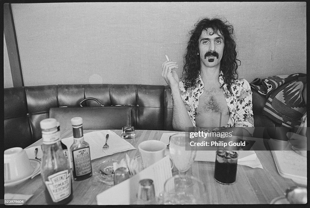 frank-zappa-sits-and-smokes-at-a-diner-table-which-is-littered-with-various-glasses-and.jpg