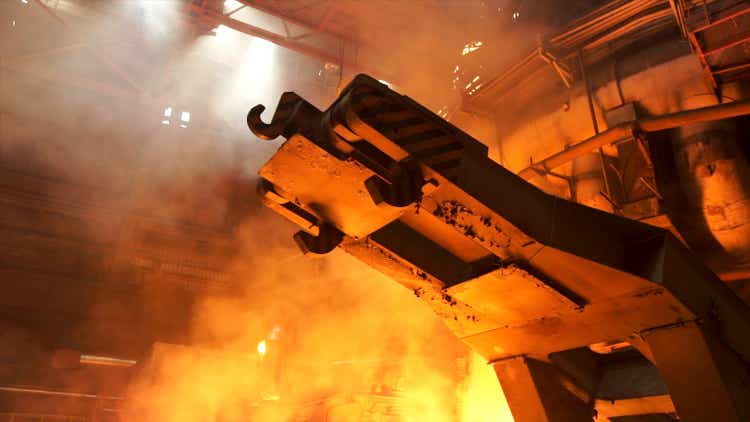 A mechanism with hooks in the hot shop with rising smoke and burning fire at the metallurgical plant. Stock footage. Heavy industry, equipment at the steel factory.